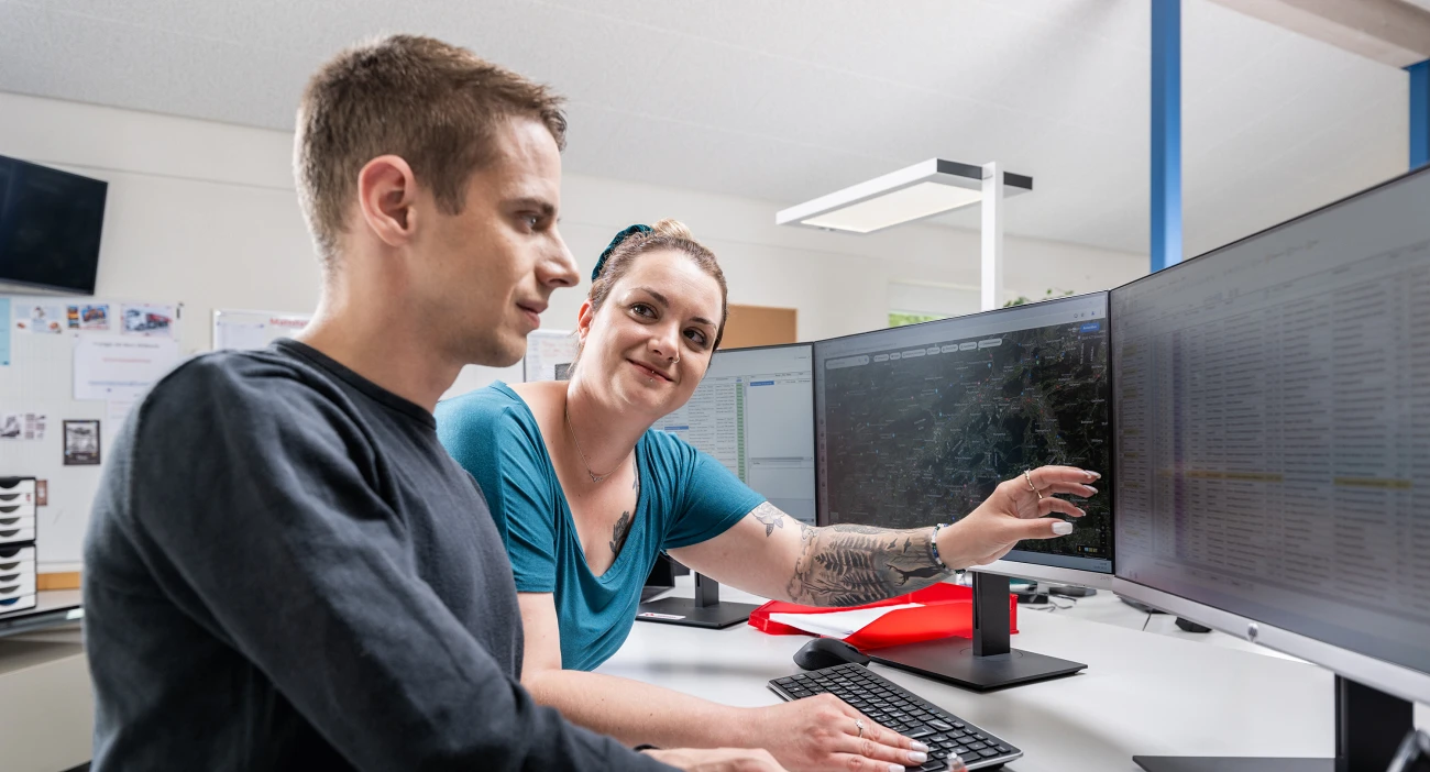 Zwei Mitarbeitende, ein Mann und eine Frau, besprechen etwas an den Bildschirmen in der Disposition